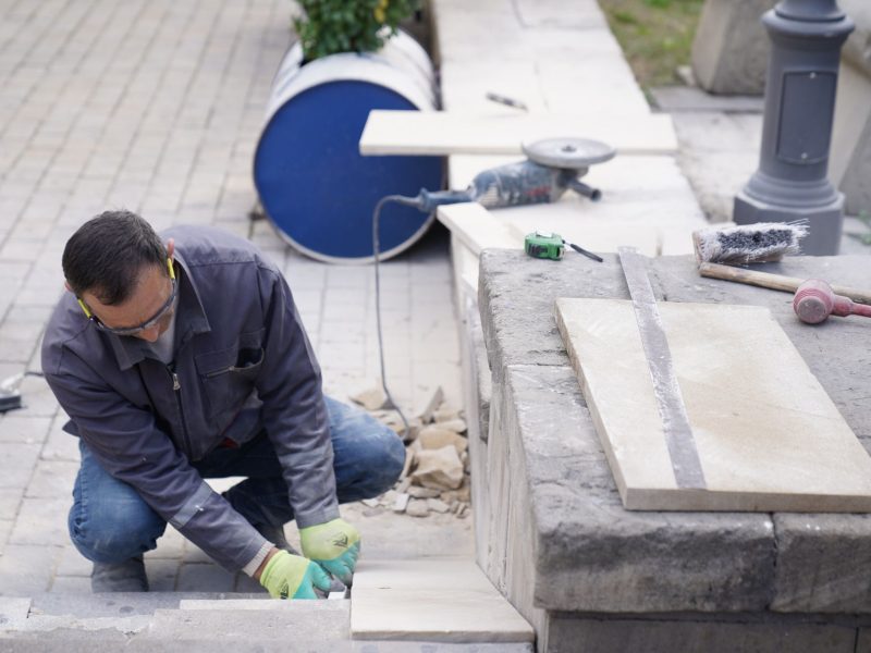 Handwerker kniet und verlegt Naturstein-Platten auf einer Terrasse
